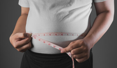Overweight or obese man with abdominal fat using a tape measure to check his waist size, Health and medicine concept He is on a diet and losing weight