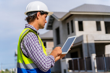Male engineer wearing hard hat using digital tablet while working on construction site.