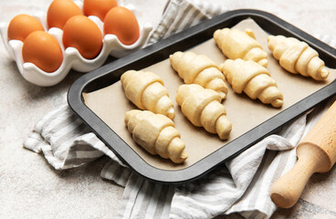 Freshly made croissants resting on baking sheet await oven's warm embrace