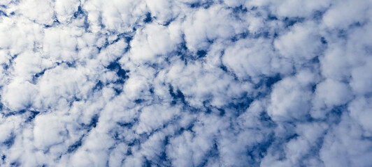 Beautiful cumulus clouds in a blue sky. The clouds form a dense, uniform pattern. One side of the sky with clouds is illuminated by the sun