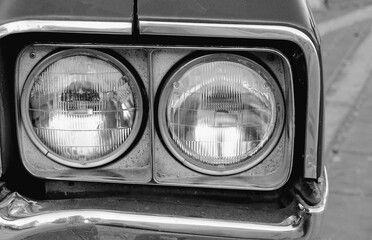 Close-up of two round vintage car headlights with chrome framing, captured in black and white from...