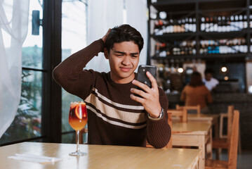 An annoyed Southeast Asian man reacts in disbelief after reading a cancellation message from his...