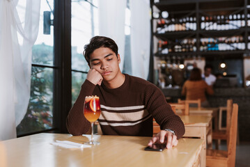 A Southeast Asian man rests his head on his hand, looking disappointed and bored while waiting...