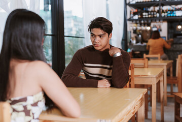 A Gen Z Southeast Asian man awkwardly adjusts his shirt during a first date that lacks chemistry or...