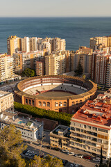 Fototapeta premium Bull Ring, Plaza la Malagueta, Andalusia, Spain. Aerial view of a historic bullring surrounded by urban buildings and a scenic coastal backdrop
