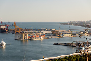 Cityscape aerial view of Malaga. Port view showcasing industrial shipping containers, cranes, and vessels in a bustling harbor environment with water reflections