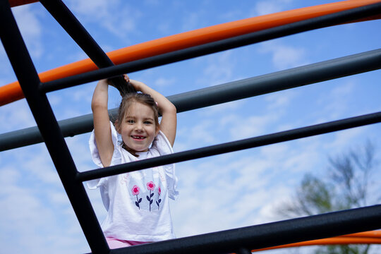 Smiling girl climbing bars at playground under blue sky