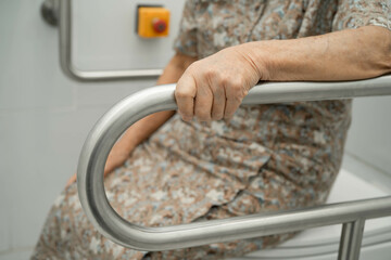 Asian elderly woman patient use toilet support rail in bathroom.