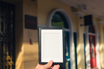 Hand holding a black photo frame with a china town background. Concept of photomontage into a beautiful frame. 