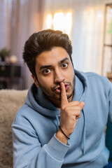 Shh be quiet please. Portrait of young Indian man presses index finger to lips makes silence...
