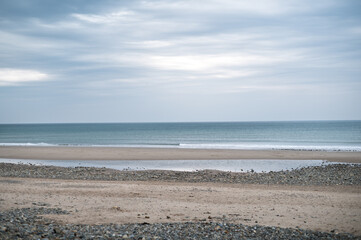 a sandy beach with stones with gentle waves lapping at the shore.