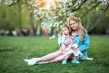 Fototapeta premium Pregnant mother hugging her daughter in a blooming apple orchard in spring