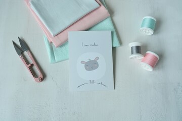Cotton fabrics, pink thread snippers, thread spools and post card with a cute dreamy sheep ion white background