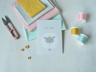 Cotton fabrics, pink thread snippers, thread spools, small wooden buttons and post card with a cute dreamy sheep in crown on white background