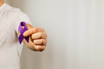 Purple ribbon held by a person against a light background for awareness