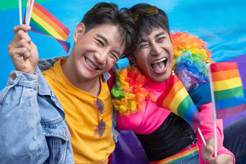 Two LGBTQ people dressed in colorful outfits have fun while waiting for the Pride parade. holding a...