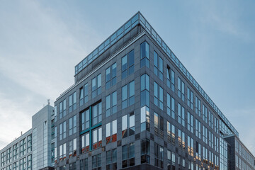 Fototapeta premium A sleek, modern office building with a glass and steel facade stands prominently against a soft blue evening sky. 