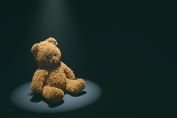 Teddy bear with torn eye illuminated by spotlight sits in dark room. Child abuse and violence concept.
