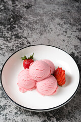 Scoops of pink strawberry ice cream, served with fresh strawberries on a white plate