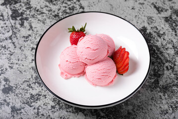 Scoops of pink strawberry ice cream, served with fresh strawberries on a white plate