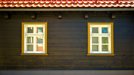 Two white windows in a yellow frame on a black wooden wall.
