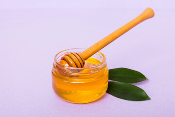 Honey in jar with leaves and honey dipper on colored background top view with copy text