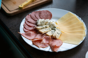 sliced cheeses and ham with sliced cheese and fresh herbs on a white plate on a wooden table.