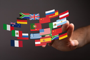 A hand interacts with a digital display of various national flags, symbolizing global connection...