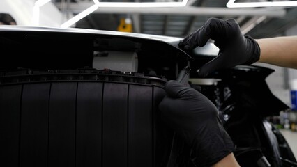 Car mechanic meticulously applying sealant along the edge of a vehicle's hood during assembly or...