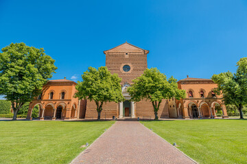 Saint Christopher Church of the Charterhouse in Ferrara city of Italy, featuring a unique cotto brick facade, rises majestically under a clear blue sky amidst lush green lawns and trees