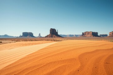 sandy desert landscape with distant mesas and clear blue sky