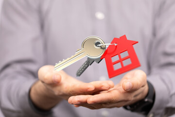 Image of house keys and a red house-shaped keychain floating above open hands, symbolizing real...