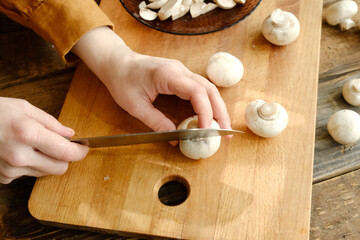 Cooking process. Hands slicing champignons mushrooms on wooden cutting board