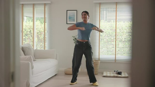 Full length young adult active black asia people Gen Z woman enjoy relax move body happy fun dancer. Humor bizarre music funny dancing crazy joy playful mental at home sofa living room with pet dog.