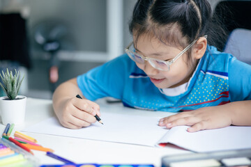 Girl wearing glasses is happily drawing on a table