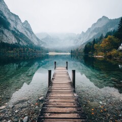 Serene lake scene; wooden dock extends into clear water beneath misty, towering mountains