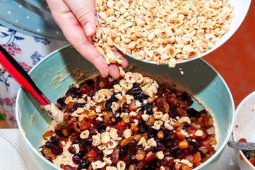 A person's hands adding chopped hazelnuts to a bowl of fruitcake batter for baking.