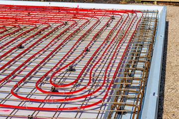 Underfloor heating system with red pipes on construction site, Close-up of underfloor heating installation using red pipes laid on a foundation grid at a building