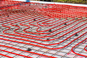 Underfloor heating system with red pipes on construction site, Close-up of underfloor heating installation using red pipes laid on a foundation grid at a building