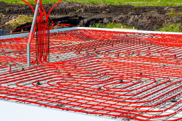 Underfloor heating system with red pipes on construction site, Close-up of underfloor heating installation using red pipes laid on a foundation grid at a building