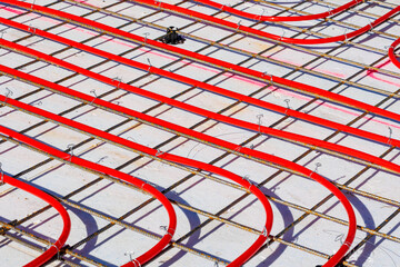 Underfloor heating system with red pipes on construction site, Close-up of underfloor heating installation using red pipes laid on a foundation grid at a building