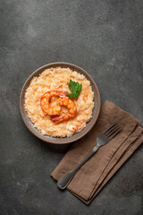 Risotto with shrimps in a bowl on dark rustic background, vertical, top view, flat lay, copy space