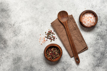 Light culinary grunge background with wooden spoon, linen napkin, peppercorns and pink salt, top view, flat lay