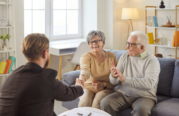 Portrait of happy cheerful senior couple sitting on couch in living room at home shaking hands with male financial advisor reaching agreement in health insurance. Investment in retirement concept