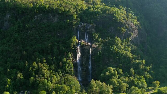 Acquafraggia Waterfalls Plunging Down On Lush Forested Cliffside In Valchiavenna, Italy. rotating drone shot, pullback