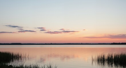Obraz premium Tranquil lake with tall grass at sunset under colorful sky 