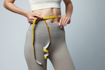 Woman measuring her belly with tape on gray background, closeup
