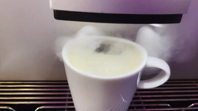 A modern automatic coffee machine is punching hot espresso. Foam and steam are coming out. Slow motion 