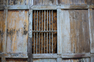 Close-up of a rustic wooden window with vertical bars and batik-patterned curtain, showcasing vintage Southeast Asian craftsmanship and cultural elements