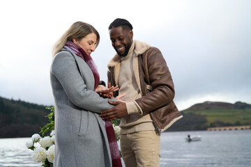 Smiling couple looking at engagement ring on woman's finger by river